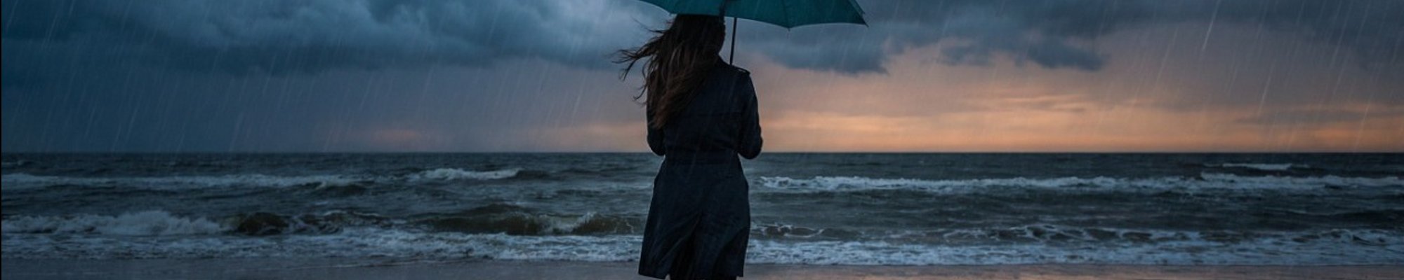 Woman standing alone on a stormy beach under a teal umbrella